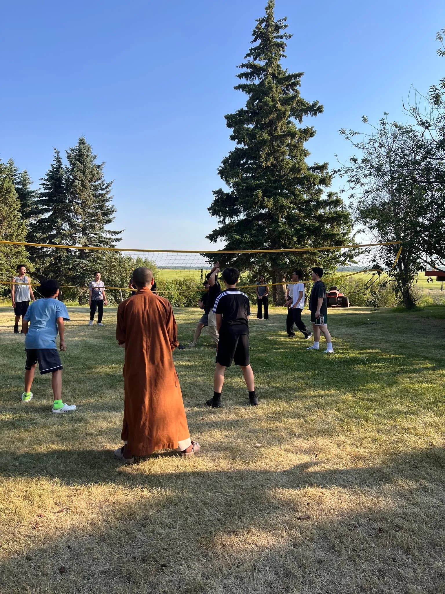 A volleyball game on the lawn, with a monk in robes looking on.