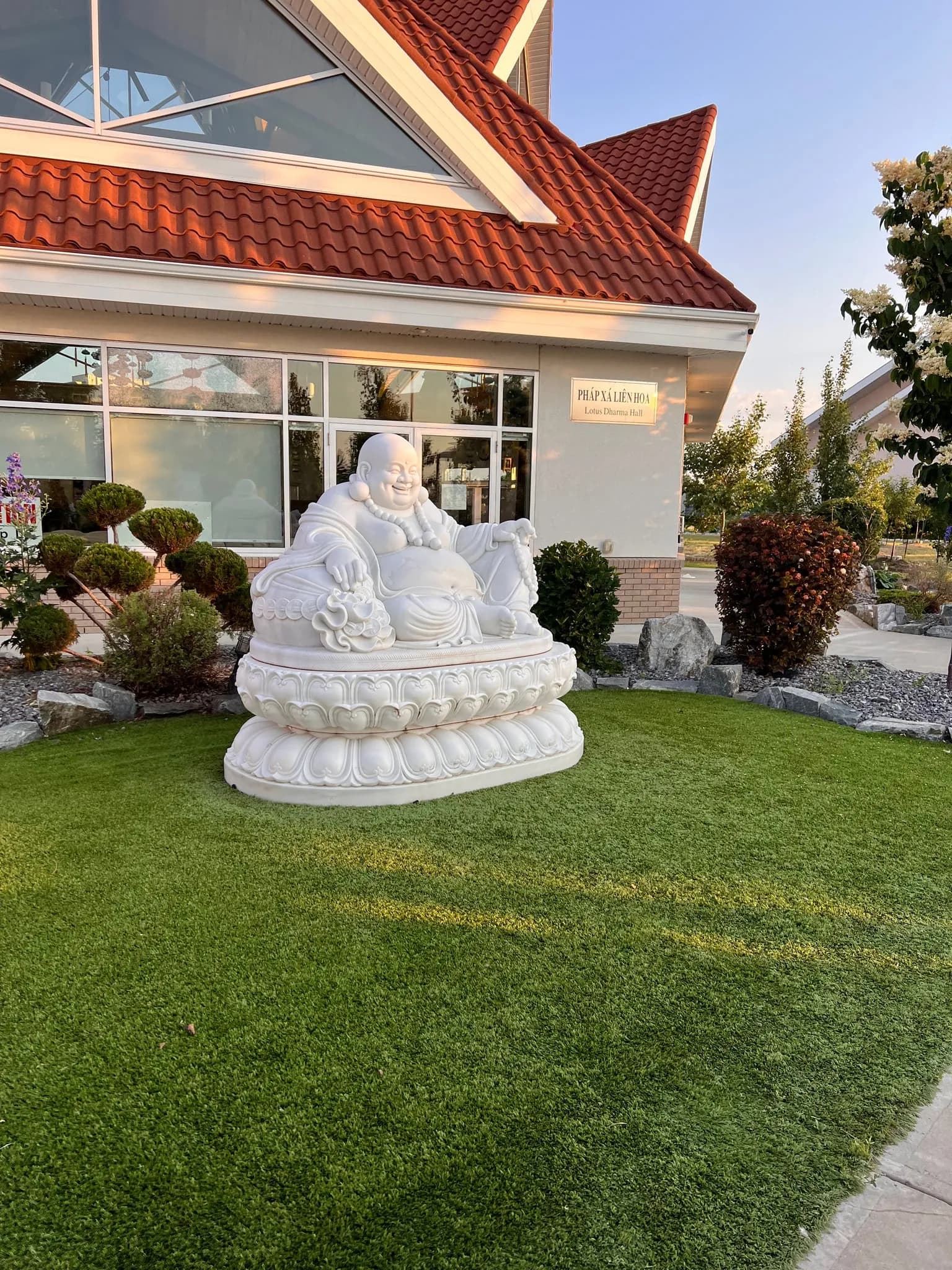 A white laughing Buddha statue outside a temple building.